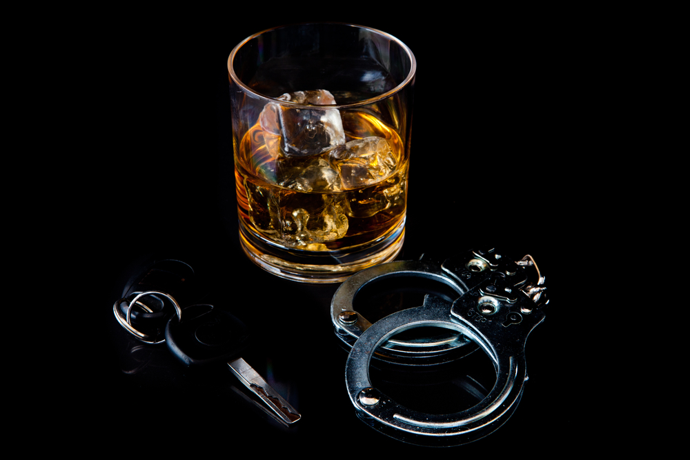 Whiskey on the rocks with handcuff and car key against a black background
